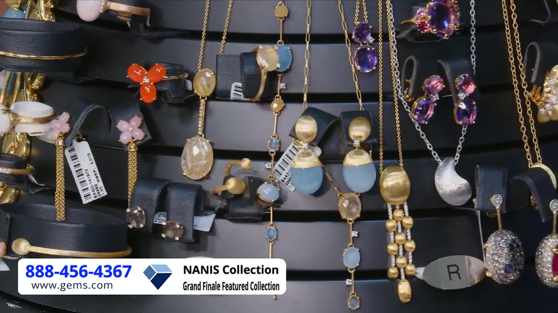 Jewelry hangs on black display stands, the gold chains catching the light. The Gem Shopping Network logo is in the bottom left corner, and the phone number is prominently displayed.
