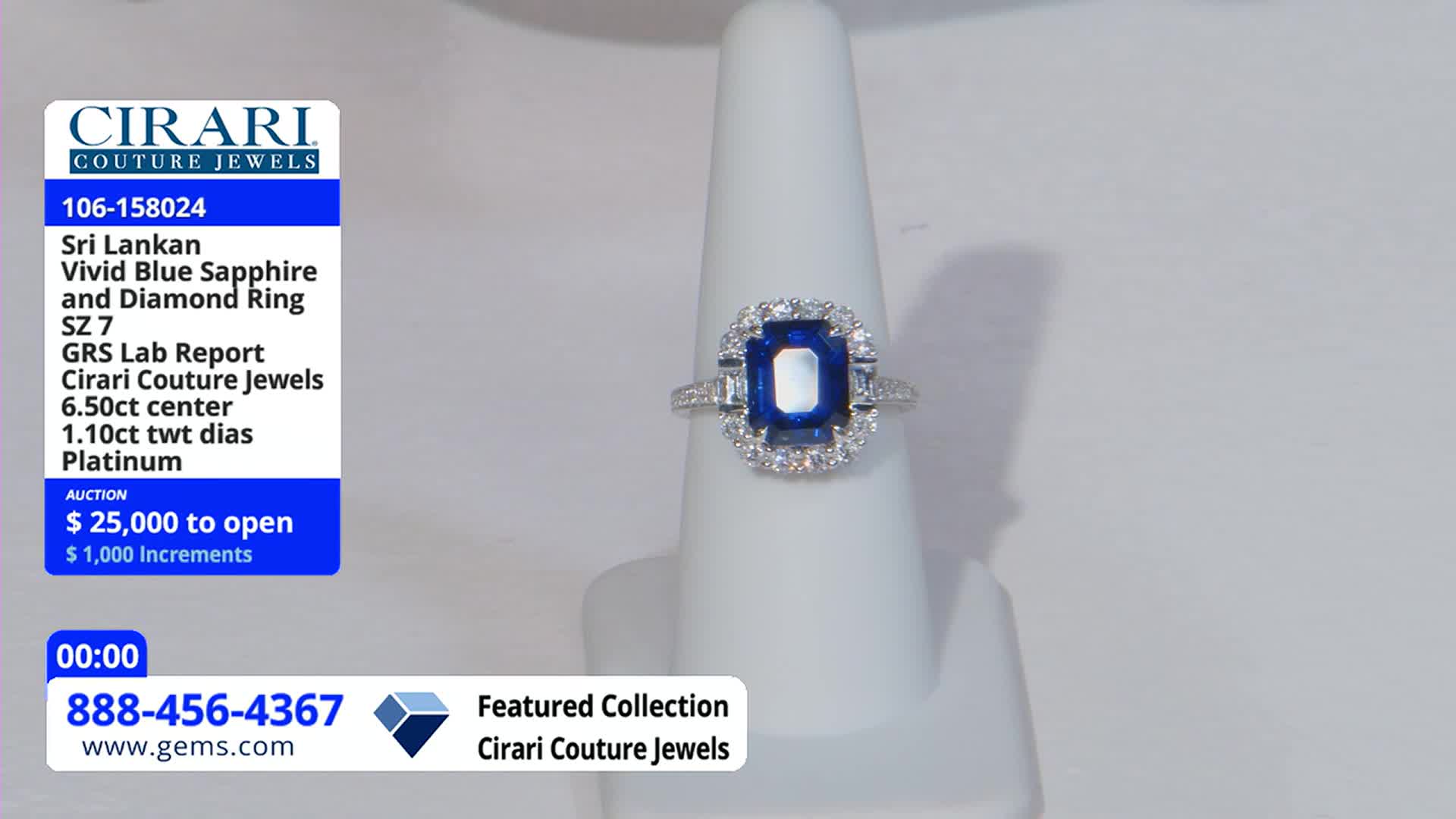 A platinum ring with a large, vivid blue sapphire is displayed on a white stand. The Gem Shopping Network is auctioning it off, starting at $25,000.
