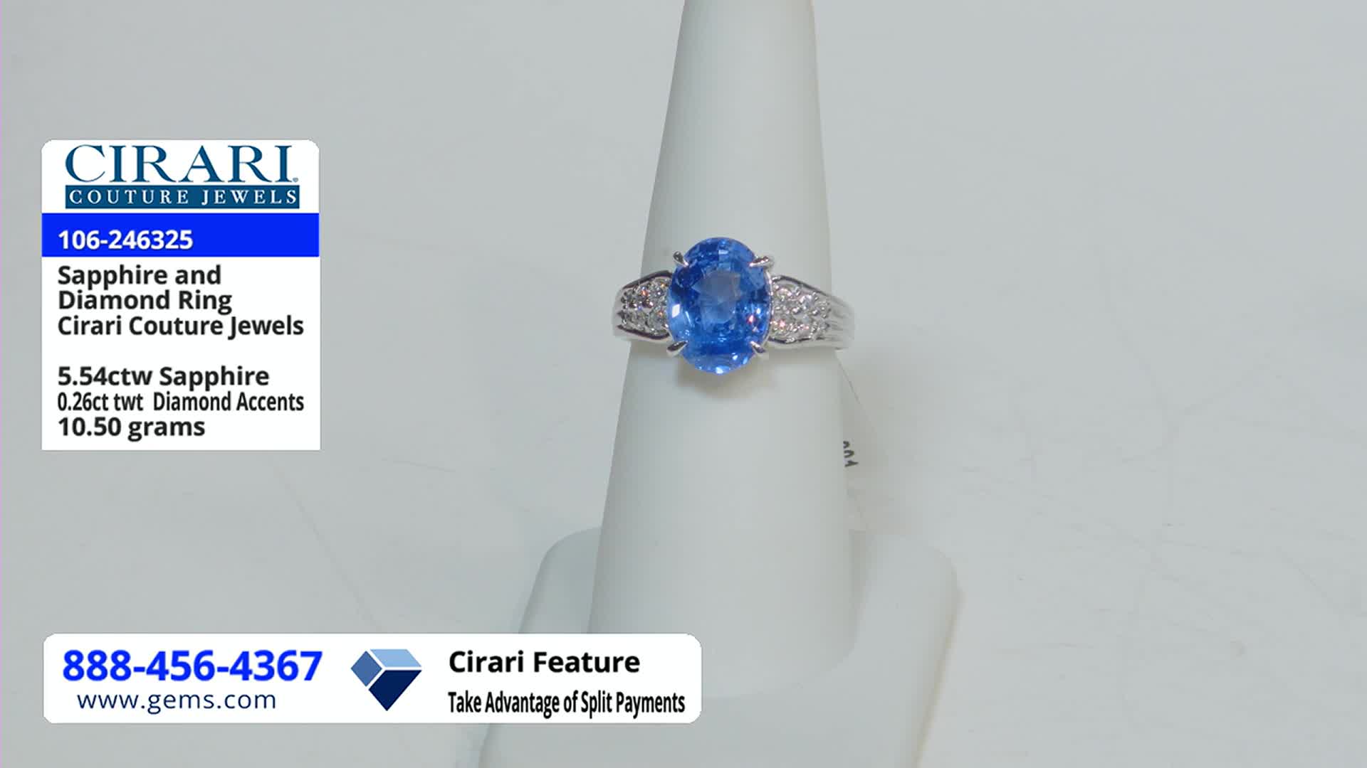 A large, oval sapphire ring sits on a white display stand. The Gem Shopping Network is advertising the ring, with details about the sapphire and diamond accents on a nearby card.
