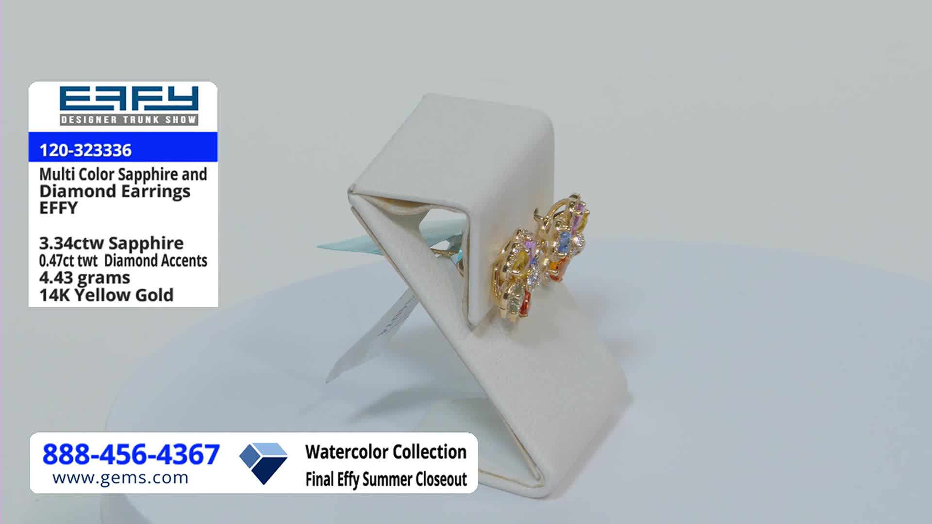 On a white display, a pair of gold earrings with colorful stones sits angled toward the camera. The Gem Shopping Network logo and product details are visible in the background.
