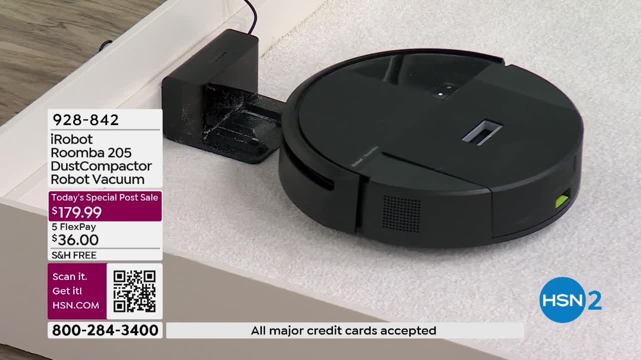 The iRobot Roomba 205 is docked and charging on its base. A green light indicates it's powered up, ready for its next cleaning cycle.