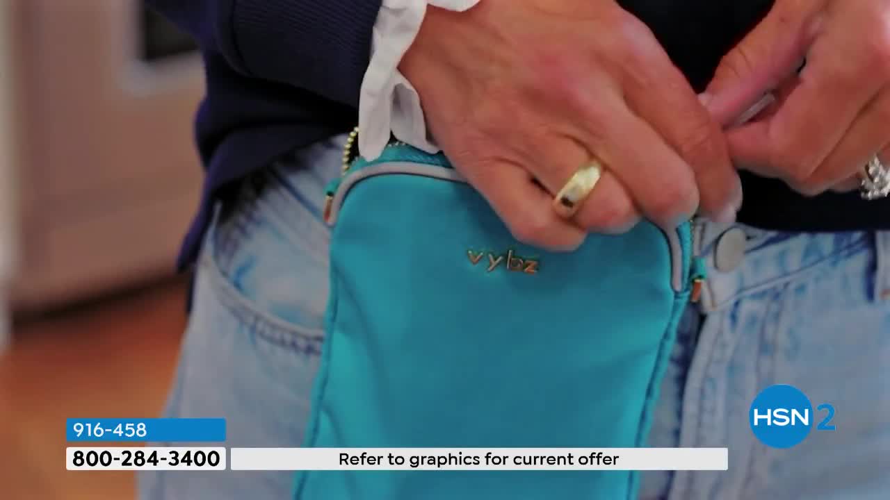Hands are adjusting a bright teal bag clipped to a pair of light-wash jeans. A gold ring gleams on one finger as it manipulates the bag's closure.