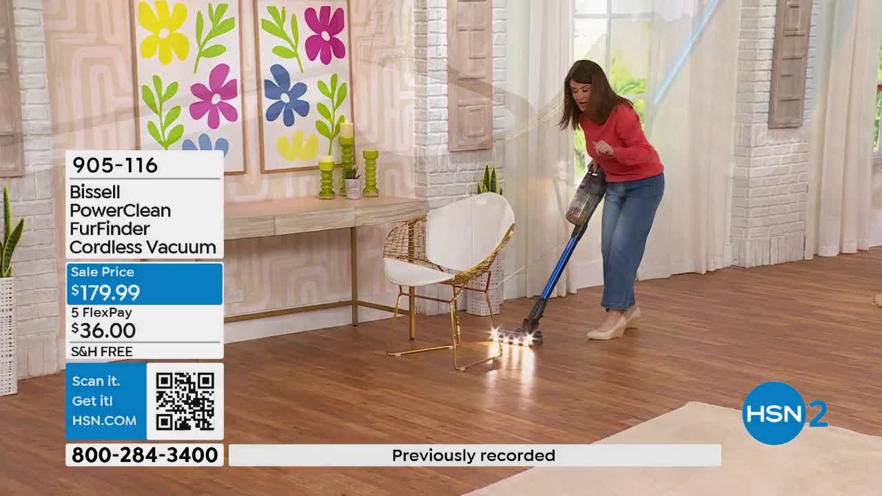 A woman in jeans and a red top demonstrates a cordless vacuum cleaner on a wooden floor. The vacuum's lights illuminate the floor as she moves it.