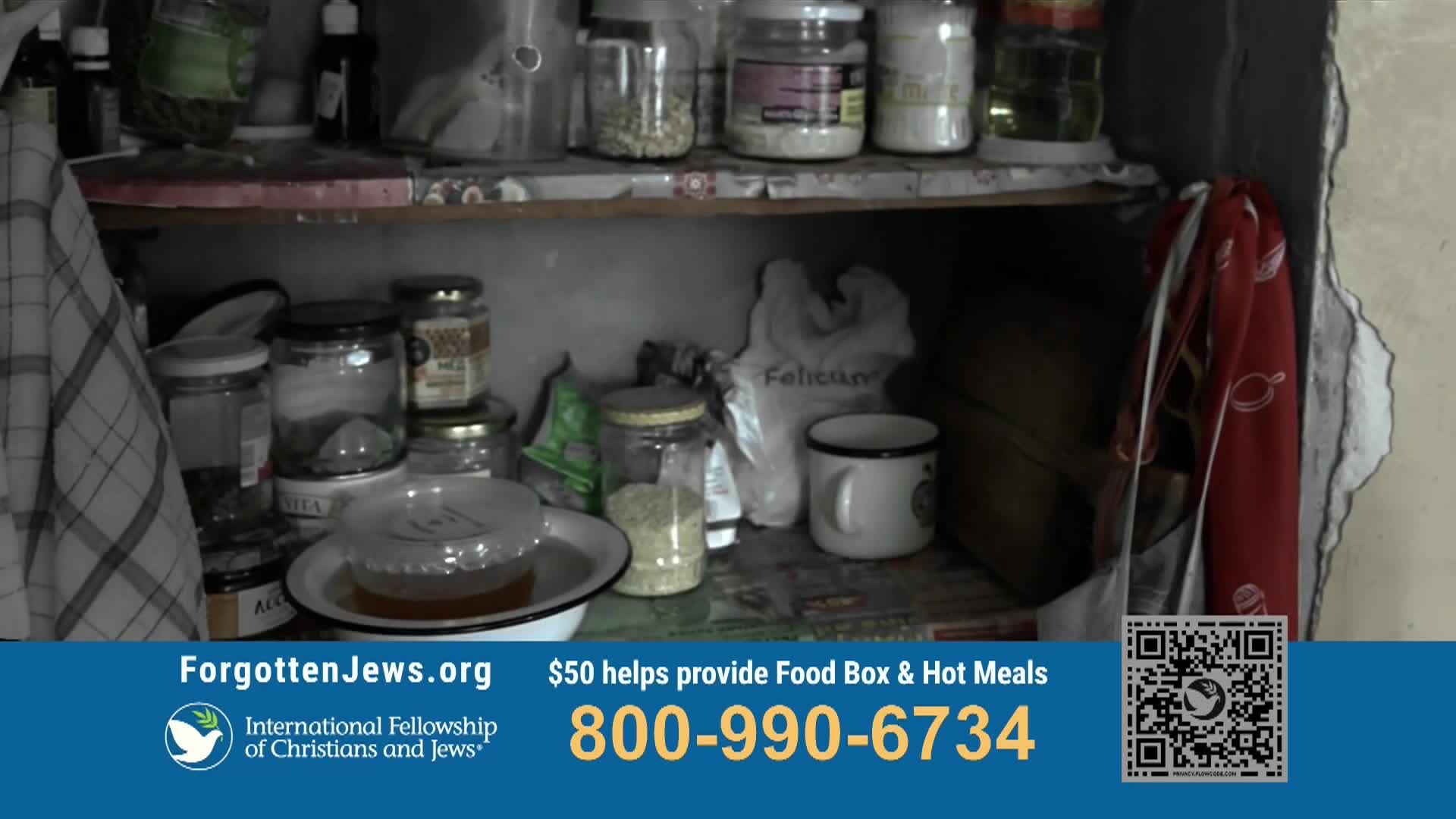 A crowded shelf holds various jars and containers, some filled with ingredients. A mug and a plastic bag sit on the shelf, and a red cloth hangs on the side.
