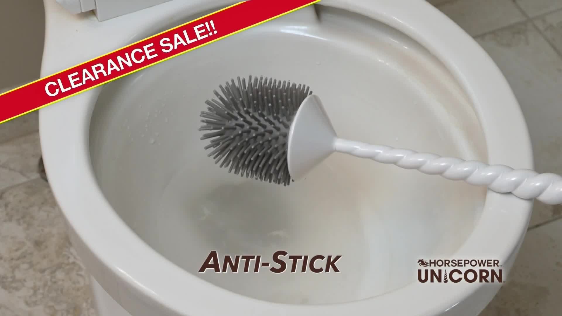 A white toilet brush with a gray head is being used to clean the inside of a white toilet bowl. The brush handle is twisted, and the image is advertising an "Anti-Stick" feature.
