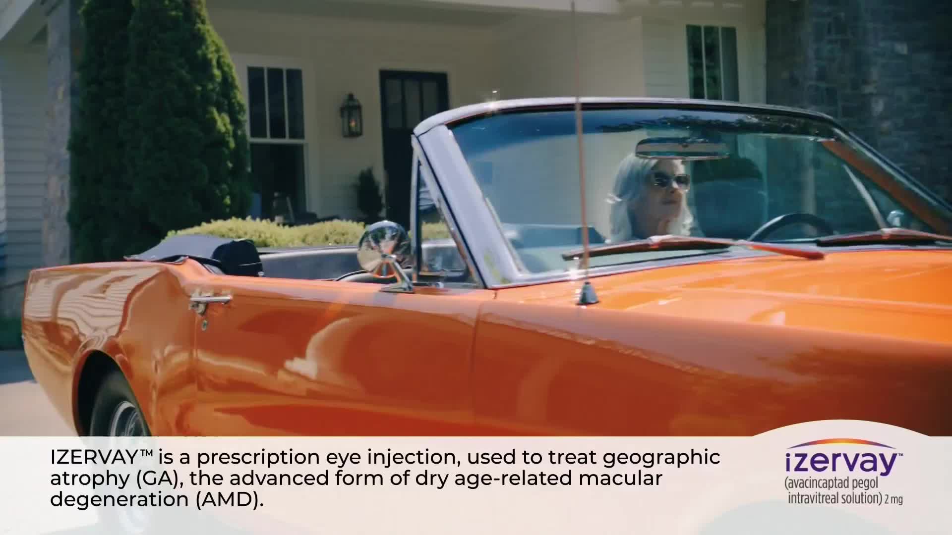 A classic orange convertible is parked in front of a house. The driver, a woman with sunglasses, is visible behind the windshield.
