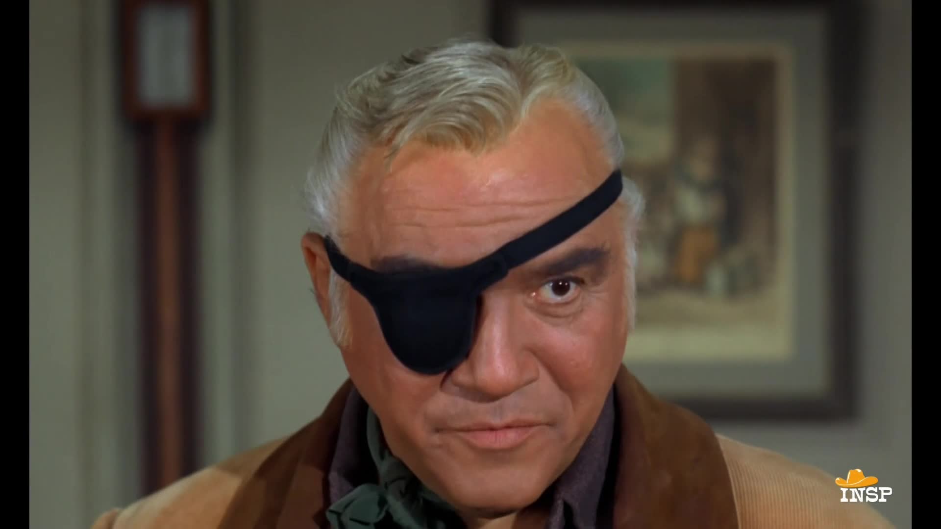 The man in the brown coat, with a black eye patch, is looking straight at me. His one visible eye is narrowed, and he seems to be sizing me up.
