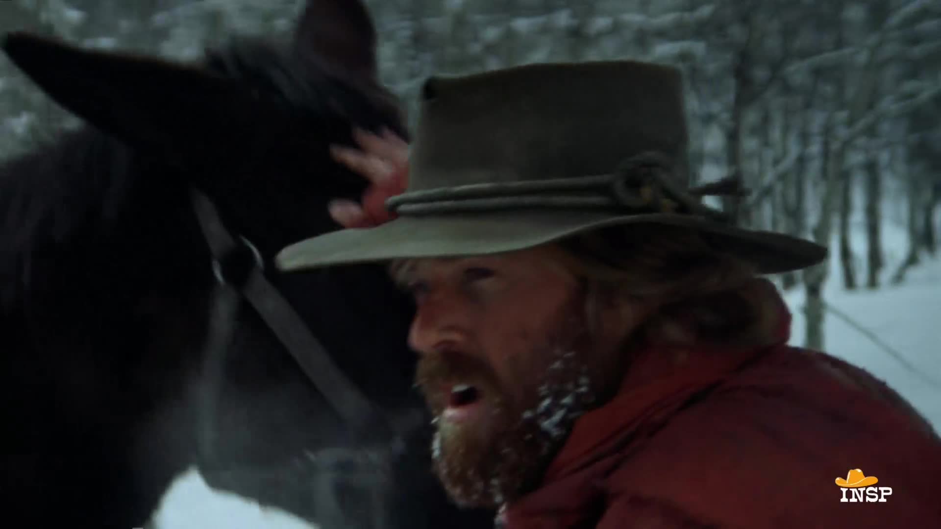 A man with a snowy beard and hat is beside a dark horse, reaching out to touch its head. The INSP logo is in the corner, likely from a Western film set in a snowy forest.
