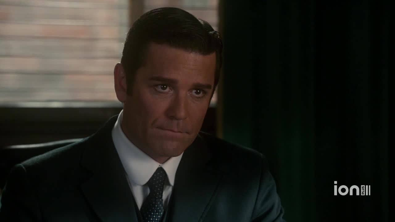A man in a dark suit sits at a desk, his gaze fixed on something out of frame. The ION Plus logo is visible in the corner.
