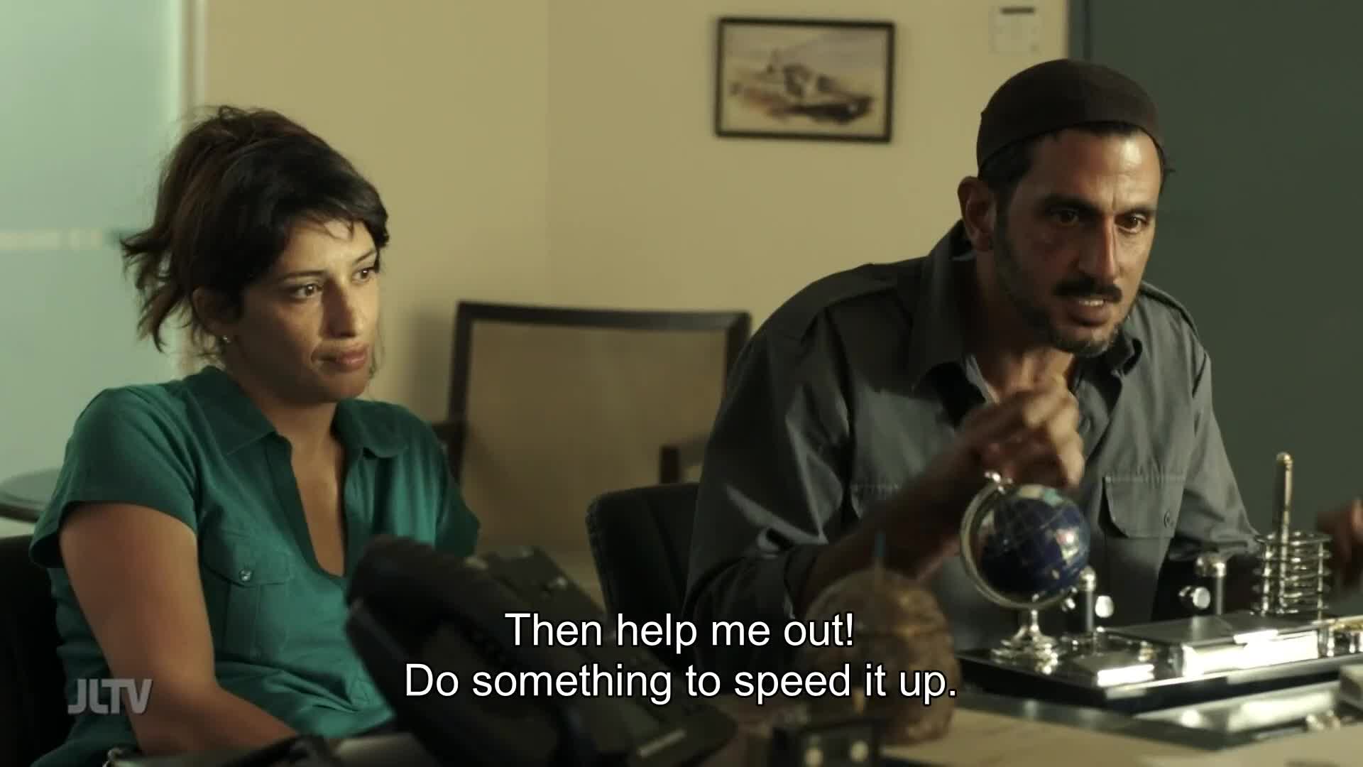 A man in a kippah gestures emphatically, his words subtitled on Jewish Life Television. Beside him, a woman in a green shirt listens intently, her expression a mix of concern and resolve.
