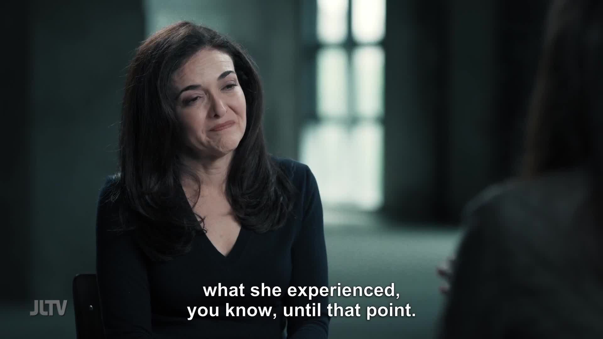 A woman with dark, wavy hair leans forward, her expression conveying a deep emotion. She speaks, her words appearing on screen as part of a Jewish Life Television broadcast from the United States.