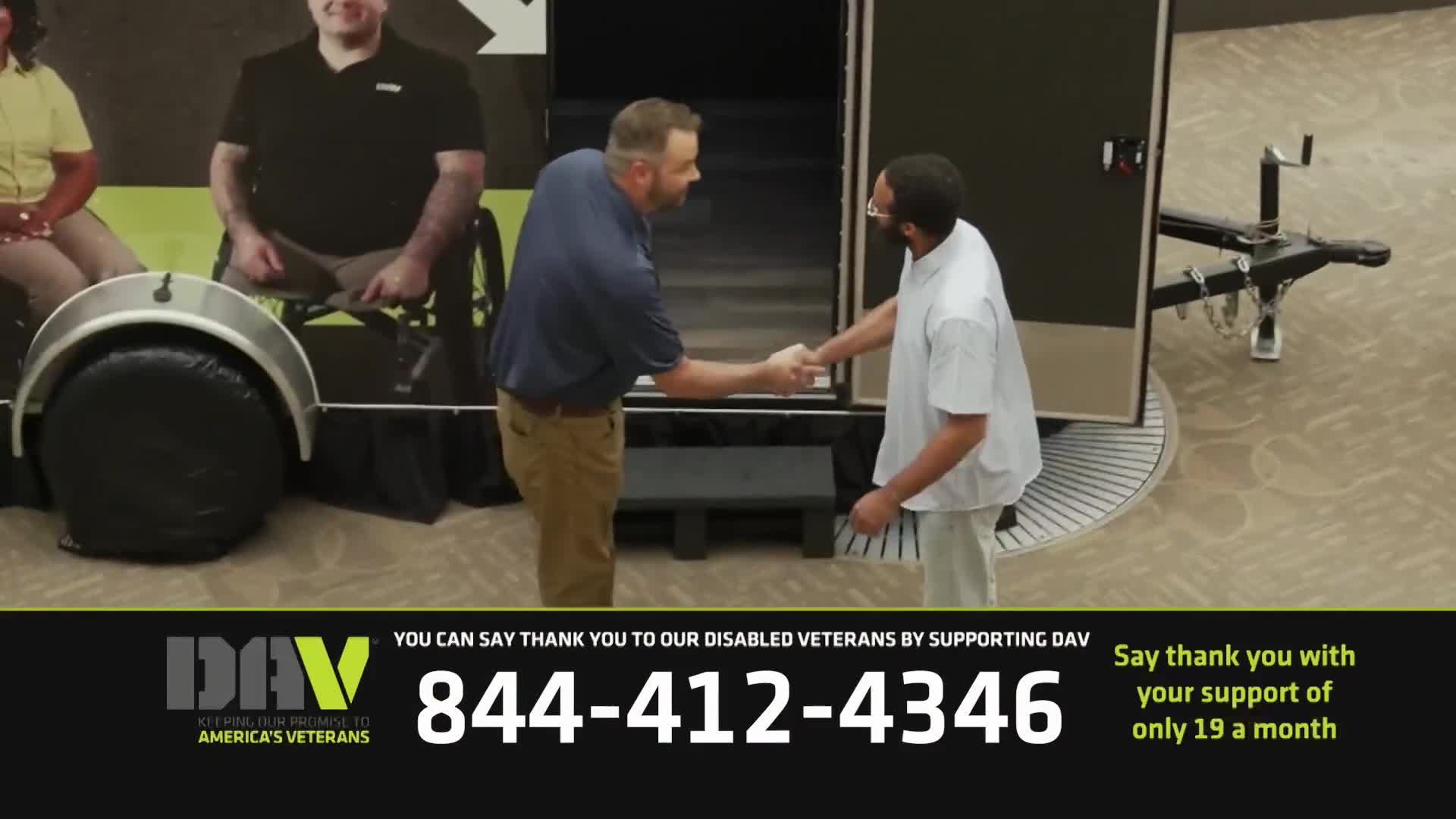 Two men shake hands in front of a trailer, one in a blue shirt and khaki pants, the other in a white t-shirt and light pants. A large graphic behind them features people sitting in wheelchairs, and a phone number for DAV, a veterans support organization, is displayed at the bottom.