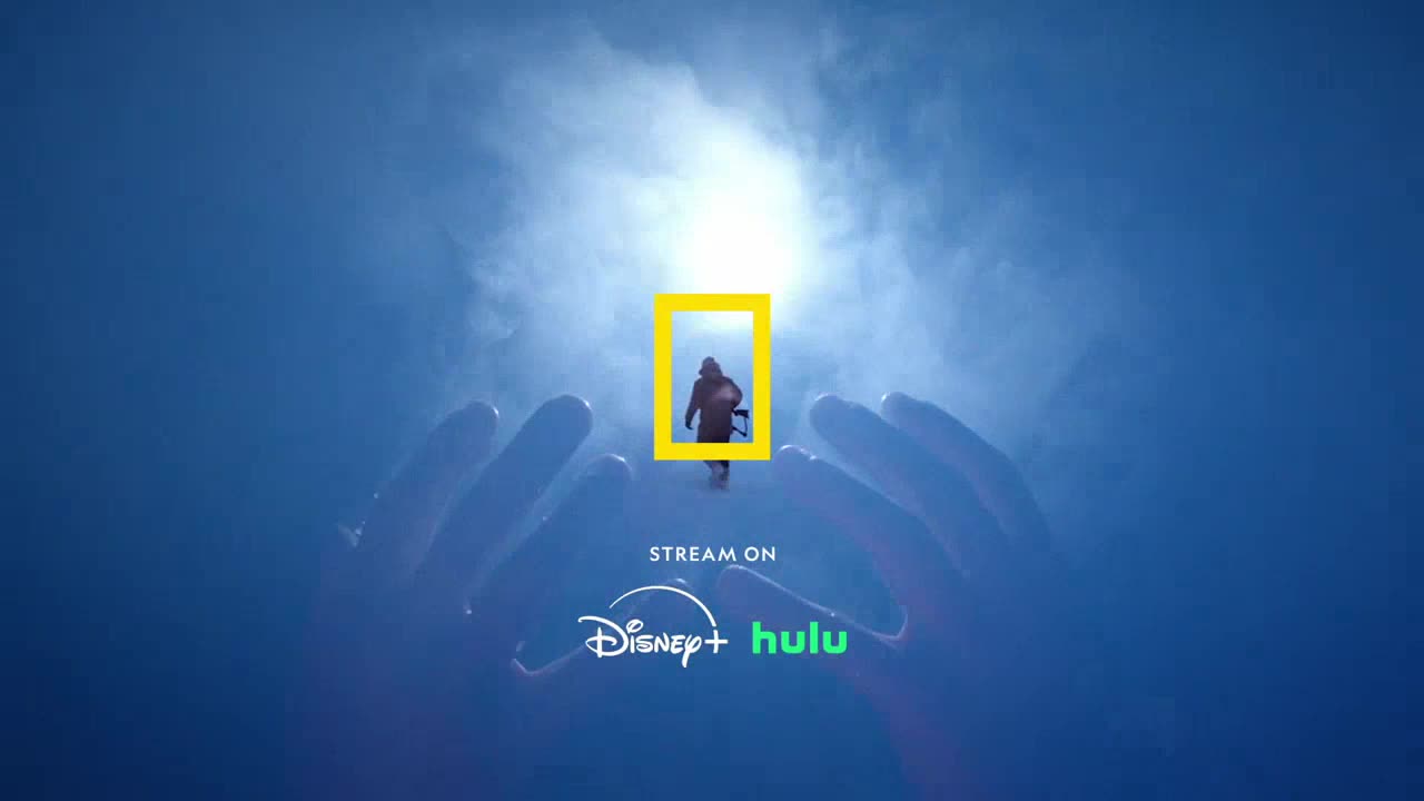 A figure walks toward the light, framed within a yellow rectangle. Giant hands cradle the scene, and the National Geographic logo is visible.
