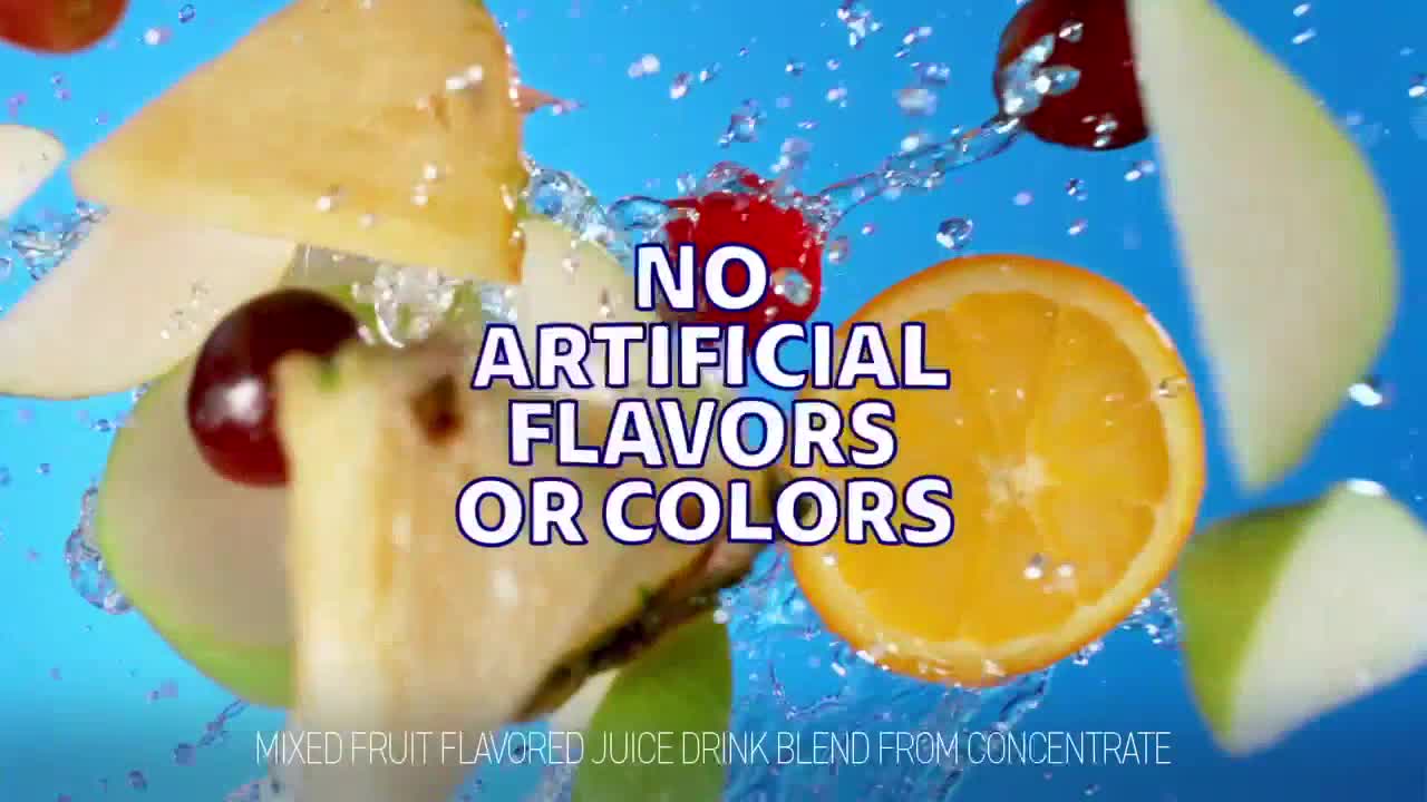Water sprays around slices of fruit, including an orange, apple, and pineapple. A cherry and a few grapes are also present, all against a bright blue backdrop.
