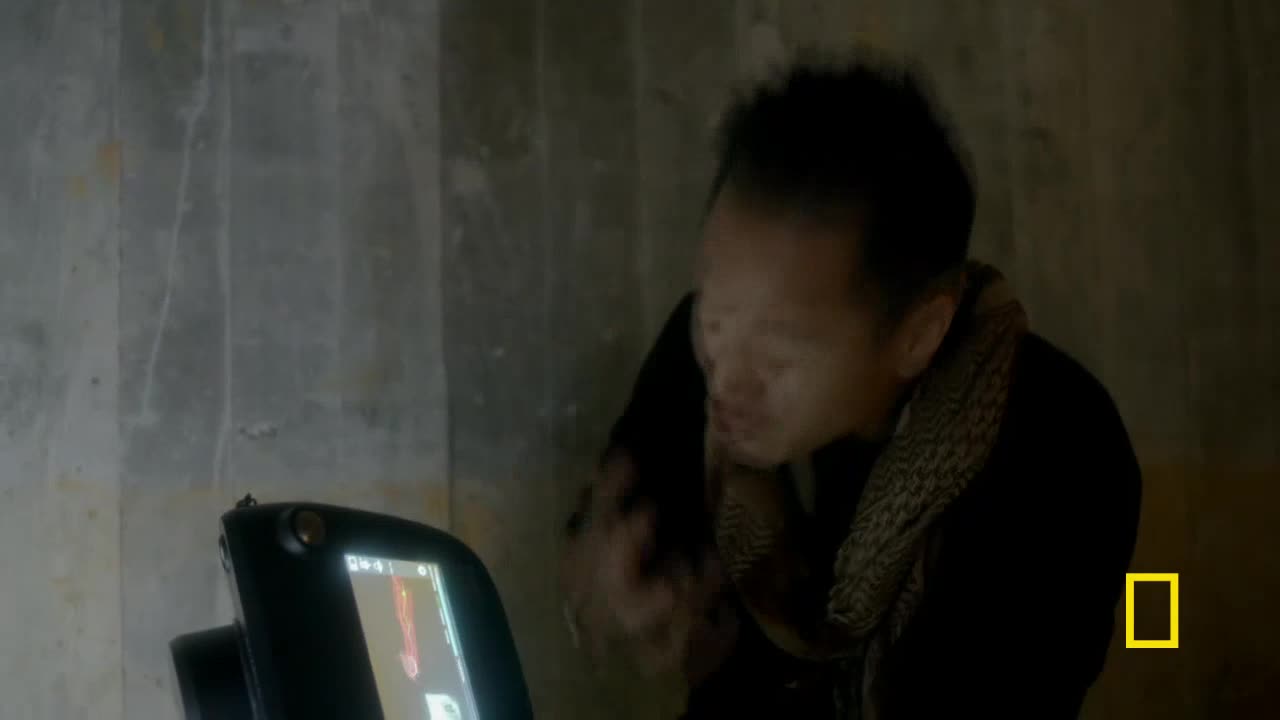 A person in a scarf gestures with their hands while looking at a screen. The National Geographic logo is visible in the corner.
