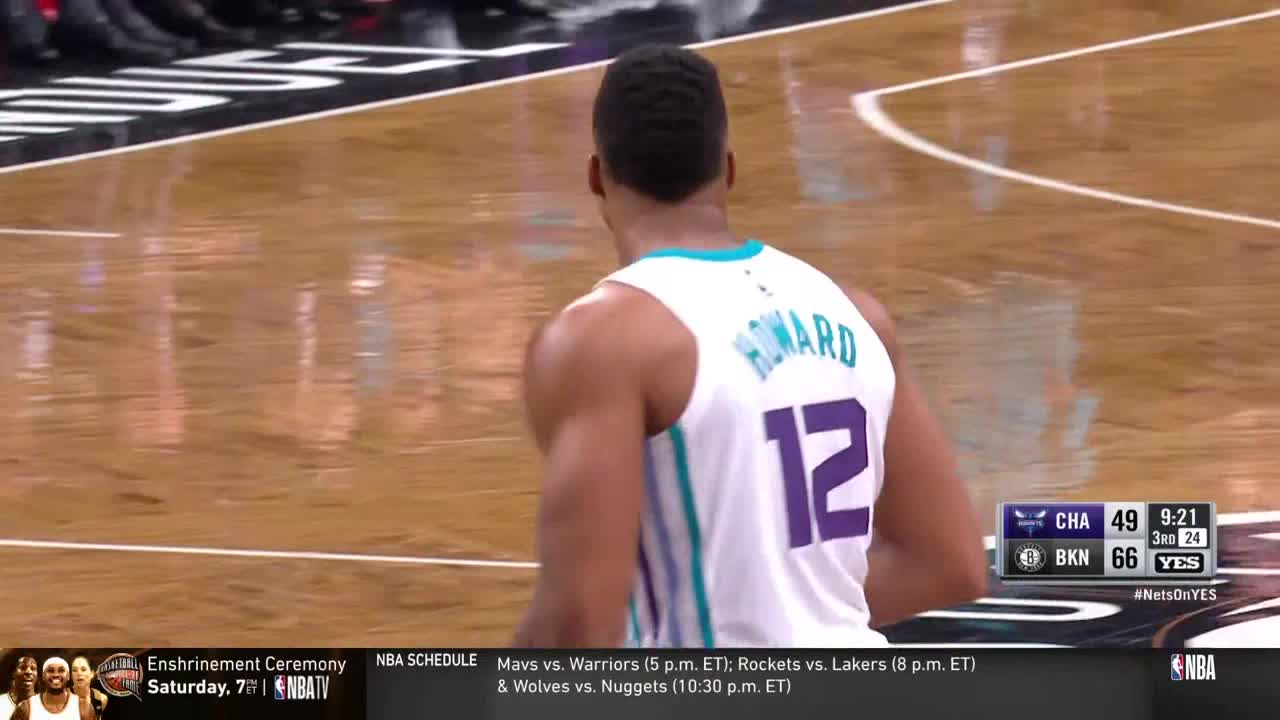 Dwight Howard, wearing number 12, stands on the court, facing away from the camera. The scoreboard shows the Charlotte Hornets trailing the Brooklyn Nets in the third quarter.
