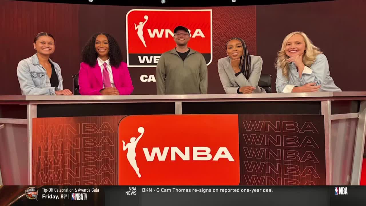 Five people are seated at a desk, smiling and looking toward the camera. A large WNBA logo is visible on the front of the desk, with NBA TV branding in the lower corner.
