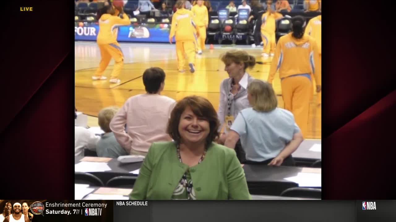 A woman in a green blazer grins directly at the camera, while players in yellow warm-up suits move around on the basketball court behind her. The NBA TV logo is visible in the corner.
