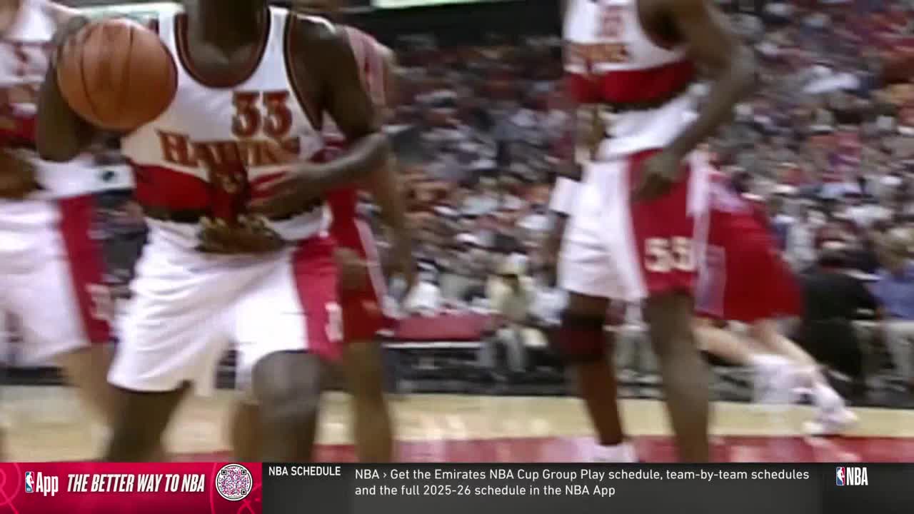 A player in a Hawks jersey dribbles the ball, his eyes focused on the court. Another player, wearing number 55, moves towards him, ready for the play.

