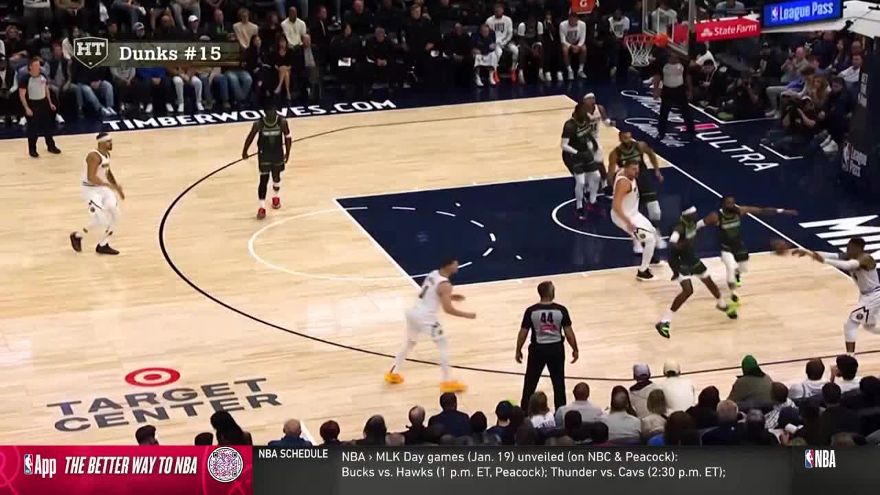 The player in white is dribbling toward the basket, while the defense in green closes in. A referee in black and white stripes watches the play unfold.
