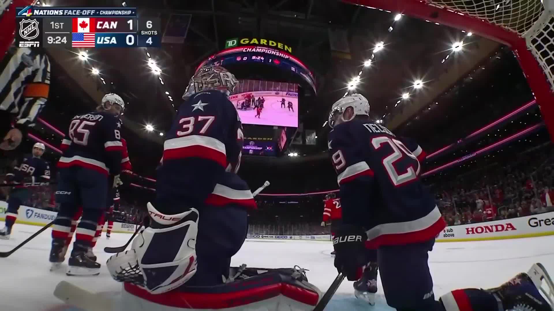 The goalie crouches, his pads a stark white against the dark ice.  A player in a navy jersey, number 29, skates past, his stick held low.
