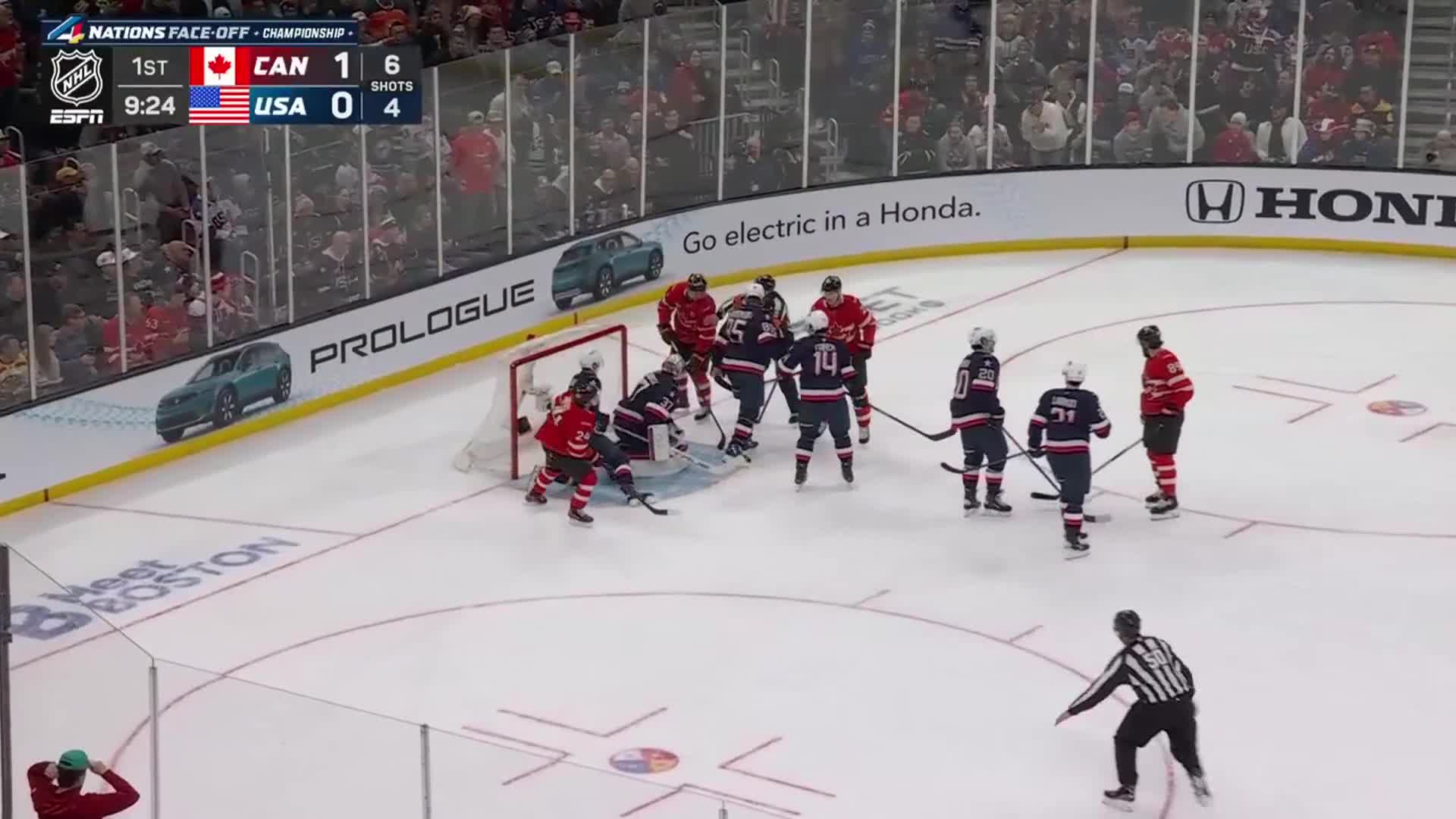 Players in red and blue jerseys swarm the net as the puck is contested. A referee in stripes watches the play unfold.