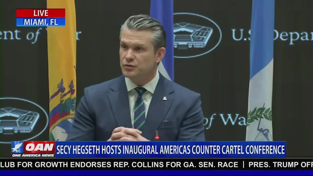 A man in a suit speaks at a podium, with flags and official seals behind him. A banner at the bottom of the screen reads "OAN SECY HEGSETH HOSTS INAUGURAL AMERICAS COUNTER CARTEL CONFERENCE."