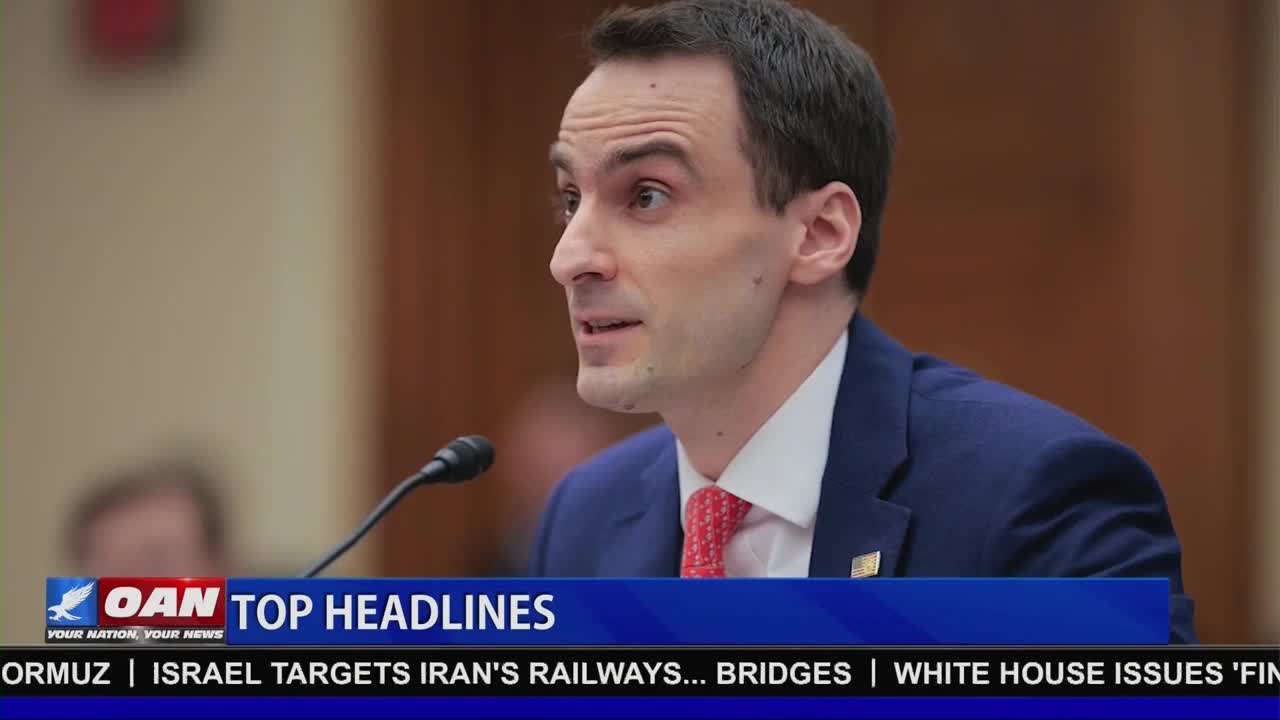 A man in a blue suit and red tie speaks into a microphone. A banner below him displays "OAN TOP HEADLINES" and text about Iran and the White House.