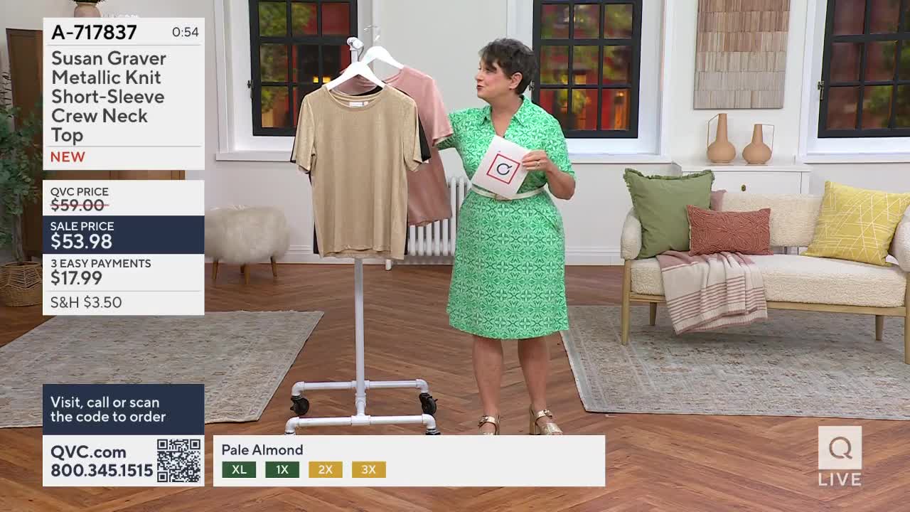 A woman in a green dress holds up a card as a metallic knit top hangs on a rack. The QVC logo appears in the bottom right corner.