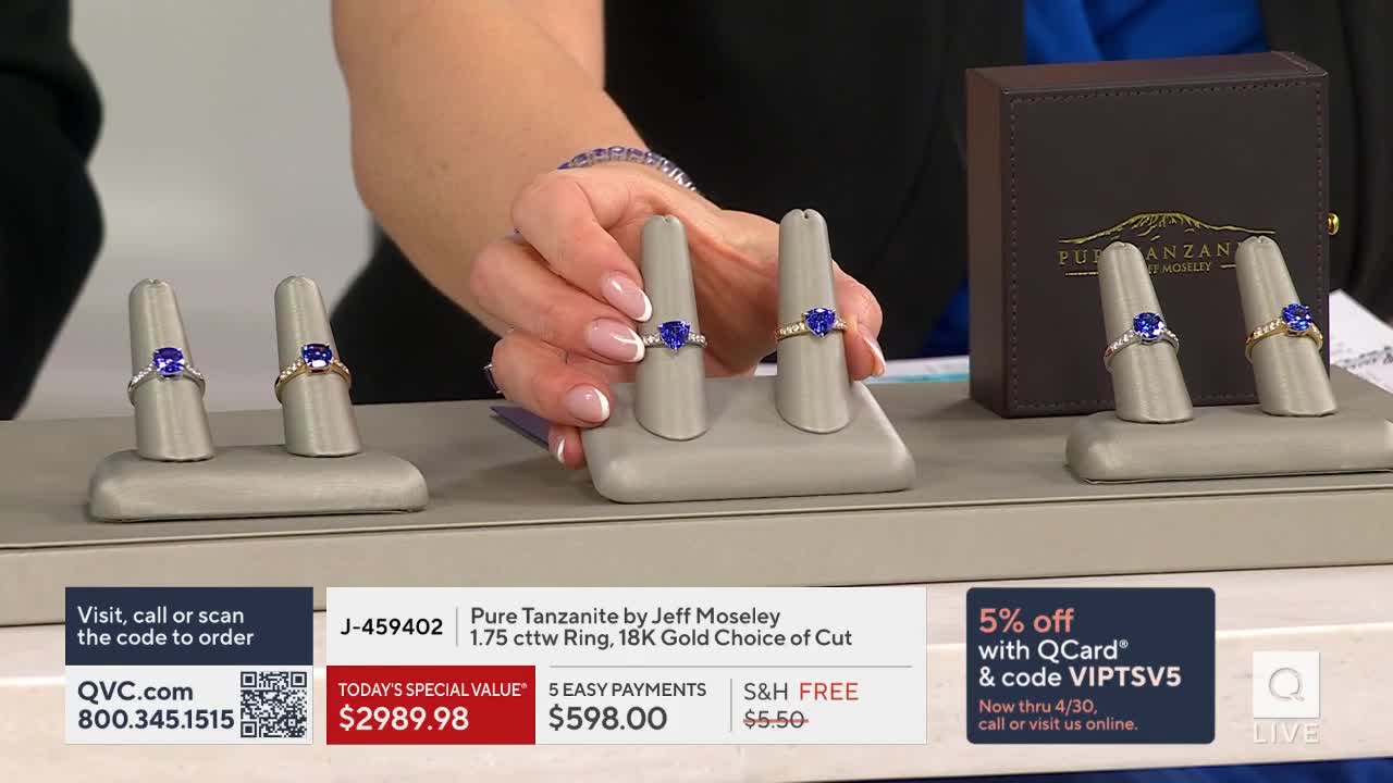 A hand holds up a ring with a deep blue stone, its band sparkling with tiny diamonds. Nearby, two other rings sit on display stands, one silver and one gold, each featuring a similar vibrant gemstone.