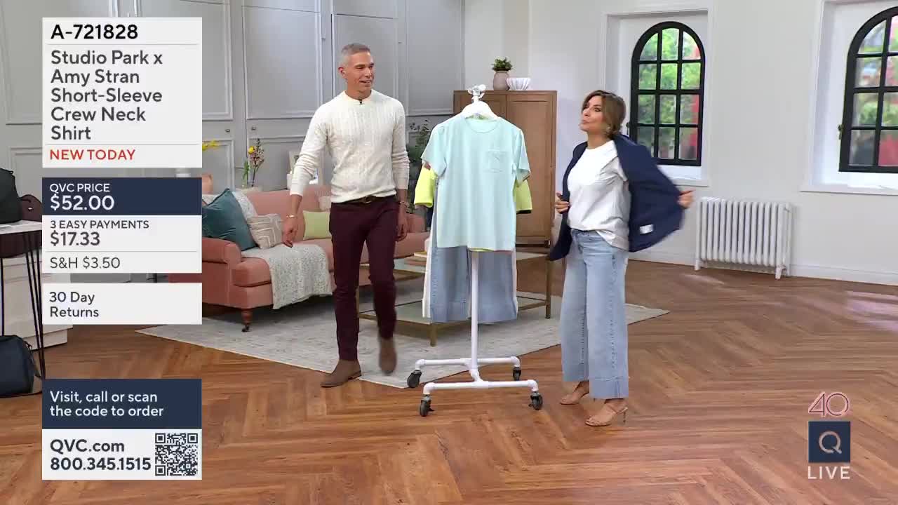 A man in a cream sweater and burgundy pants walks past a rack of t-shirts. A woman in a white tee and light blue jeans adjusts her navy blazer.