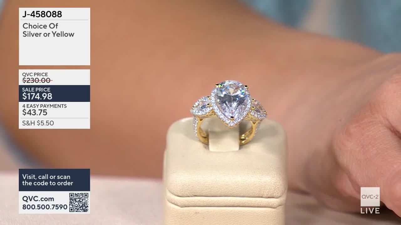 A large pear-shaped diamond ring sits on a display stand, its gold band catching the light. On the left, a screen shows the item number J-458088 and pricing details for this QVC2 offering.