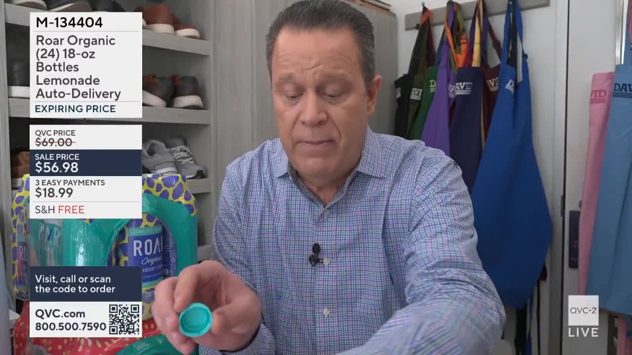 A man holds up a small, teal cap. Behind him, several bottles of Roar Organic lemonade are stacked.