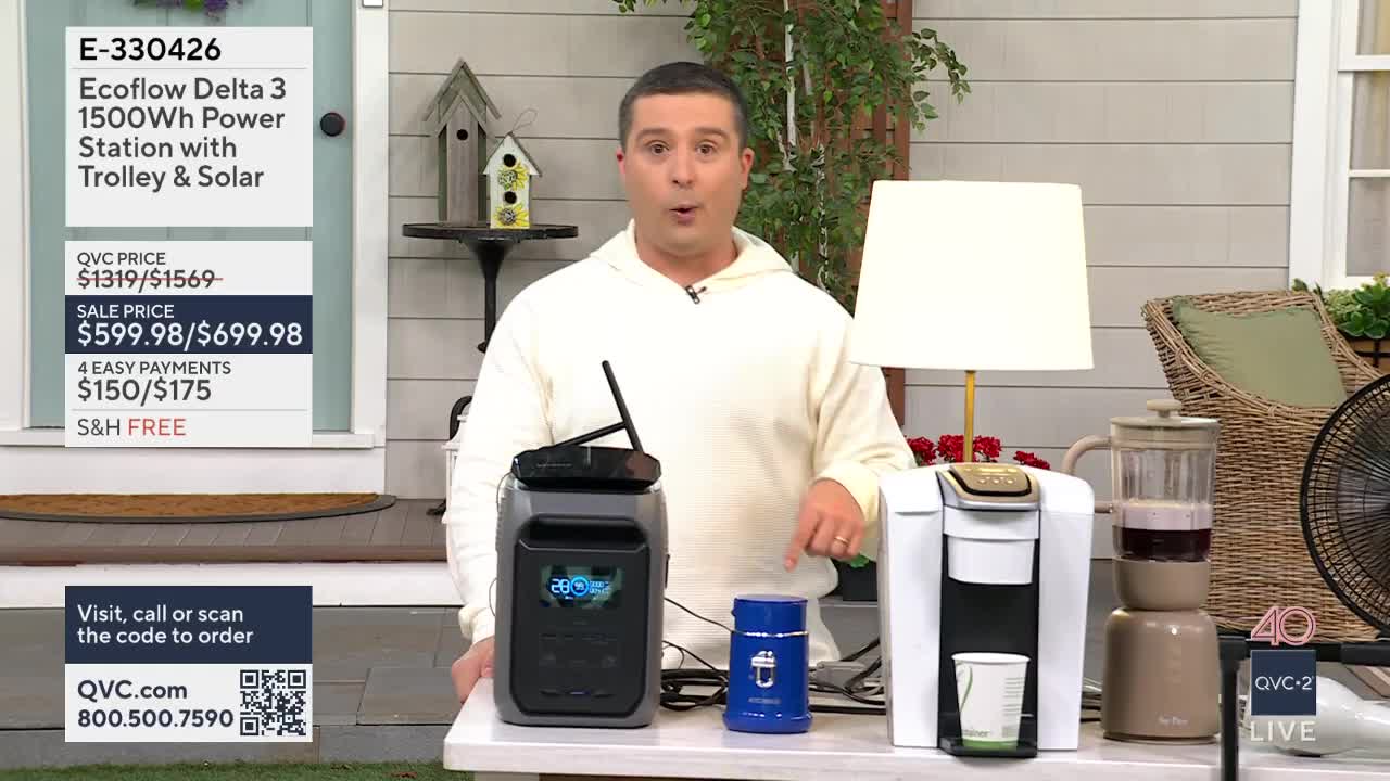 A man on QVC2 gestures toward a portable power station and a coffee maker. He's demonstrating new products for sale in the United States.