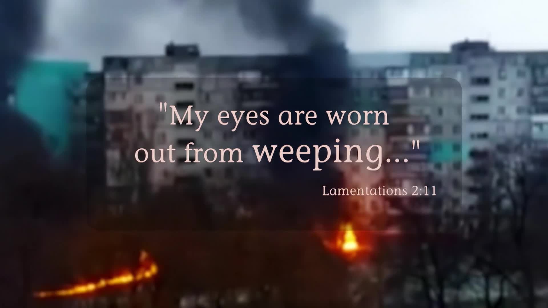 Flames lick the side of a tall apartment building, sending plumes of black smoke into the overcast sky. The windows of the structure appear dark and vacant, reflecting the orange glow of the fire.