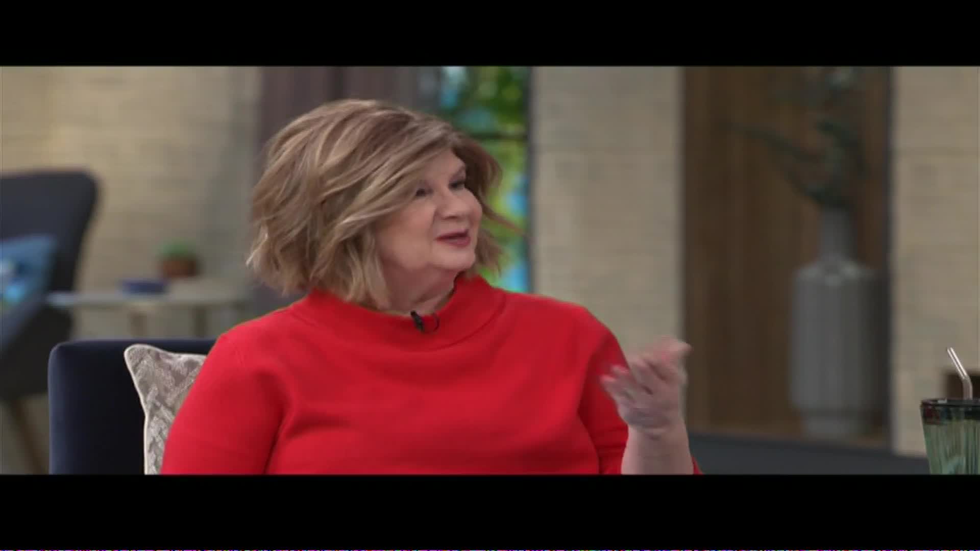 A woman in a bright red sweater speaks animatedly, her hands gesturing. She's on a set that looks like it could be for a talk show on The Word Network.