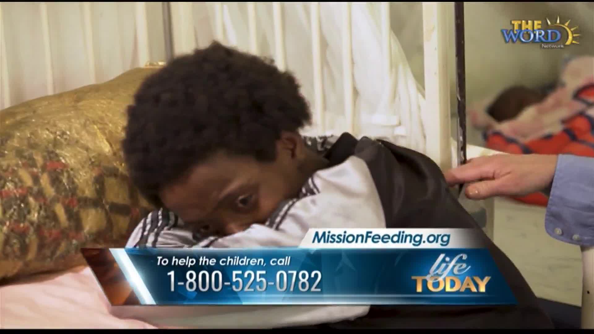 A young person rests their head on their arms, eyes wide. A hand gently touches their shoulder. A graphic overlay displays a phone number and website for MissionFeeding.org, a program from Life Today on The Word Network.