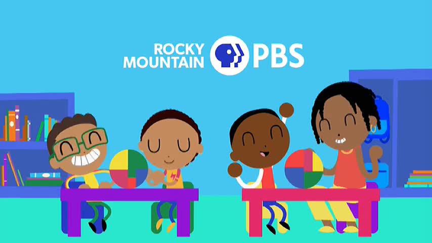 Four children sit at tables, each holding a colorful segmented ball. One child grins widely, while another raises their arm in the air.
