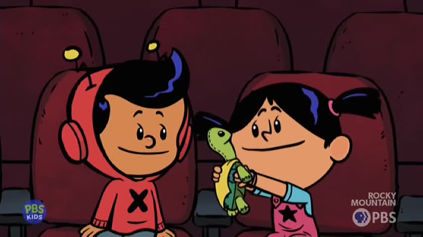 A boy in a red hoodie watches as a girl proudly holds up a small, green stuffed turtle. They're sitting in dark red seats, like at a cinema. A boy in a red hoodie watches as a girl proudly holds up a small, green stuffed turtle. They're sitting in dark red seats, like at a cinema.
