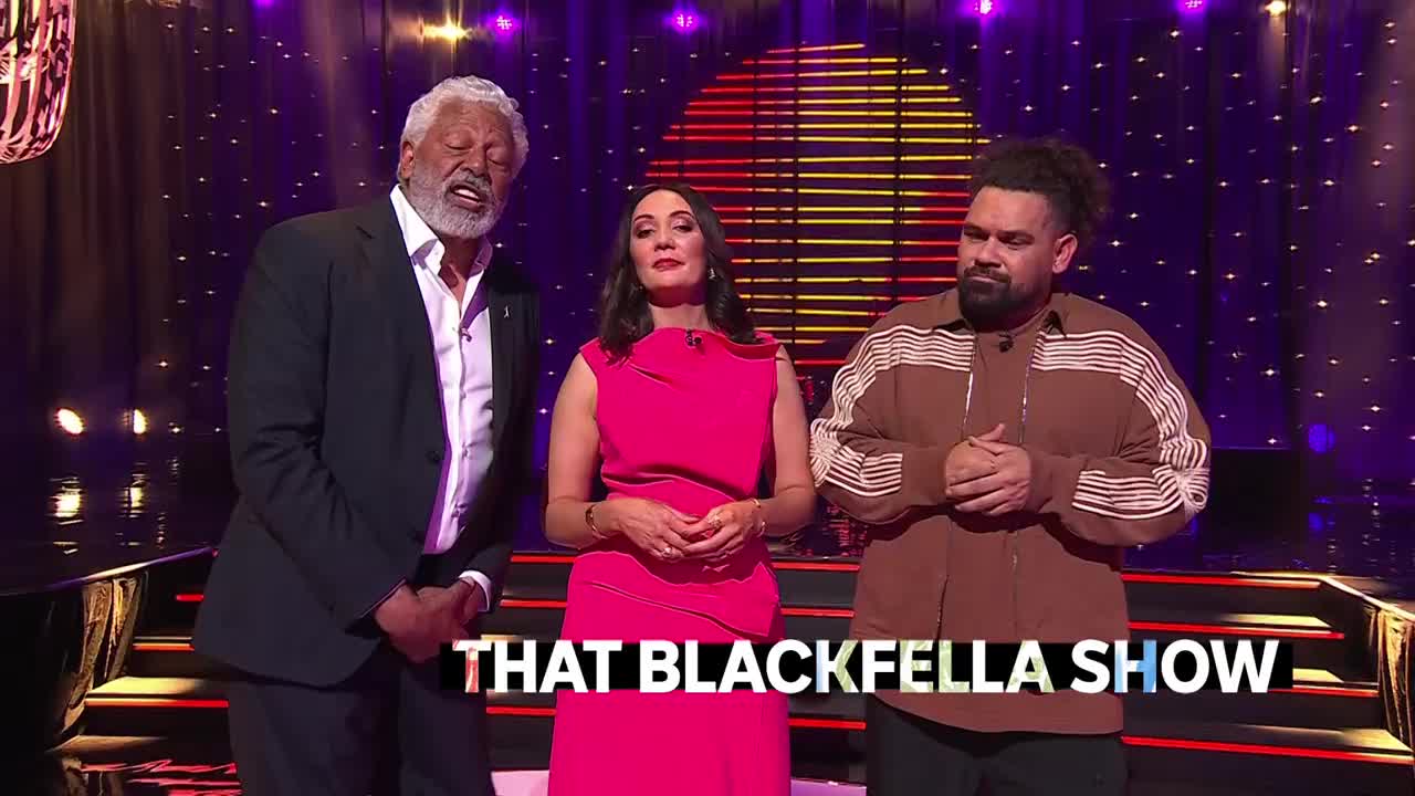 The hosts of "That Blackfella Show" stand together, the man on the left looking up as if speaking. The woman in the middle and the man on the right are looking forward, hands clasped.

