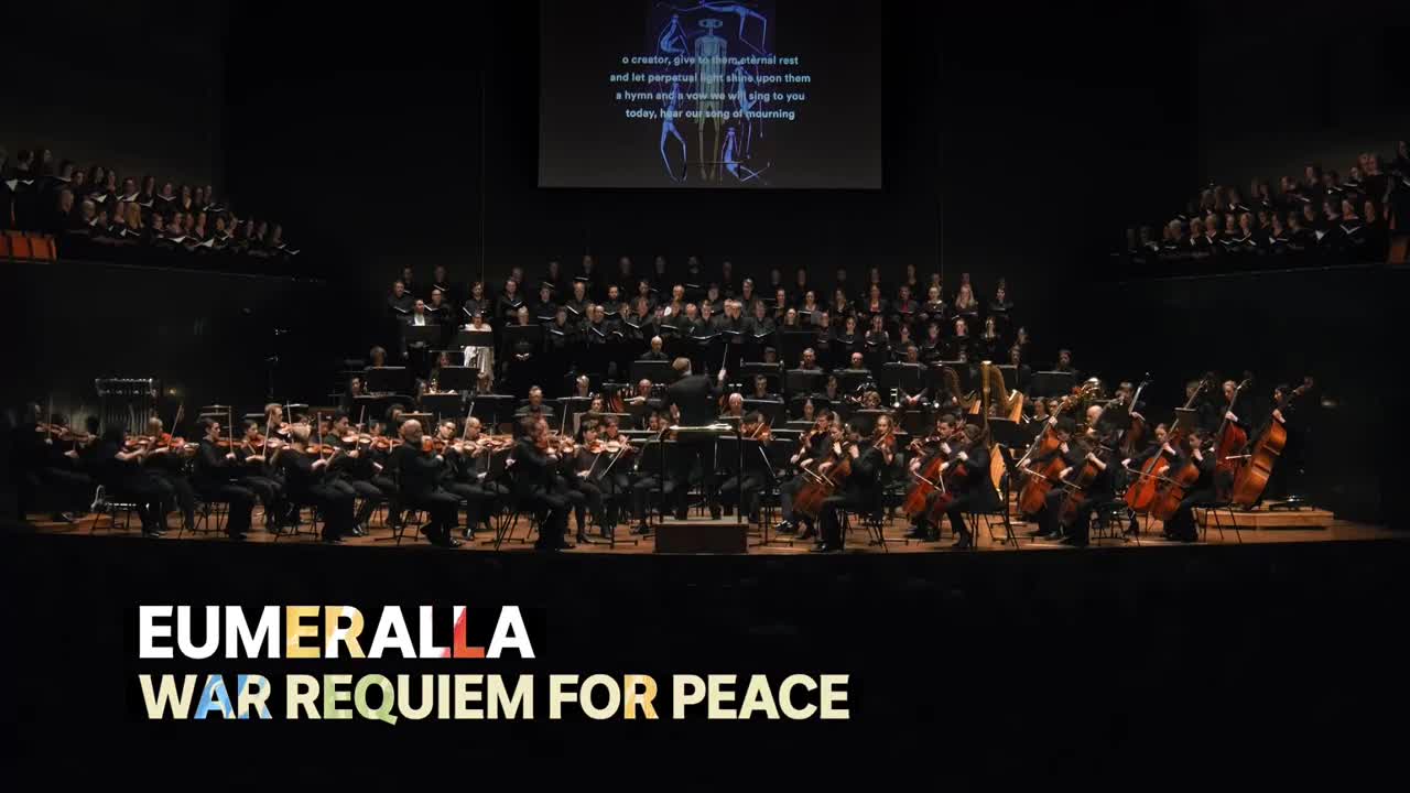 A choir and orchestra fill the stage, illuminated by spotlights. The conductor's baton moves in sweeping gestures, guiding the performance of "Eumeralla, War Requiem for Peace" on ABC Australia.

