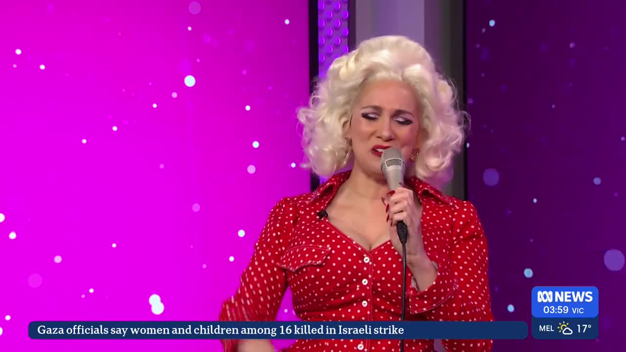 Standing here, a woman in a red polka-dot top and a blonde wig holds a microphone, her face contorted in what looks like a grimace. The ABC News logo is visible in the corner, and a news ticker scrolls across the bottom of the screen.
