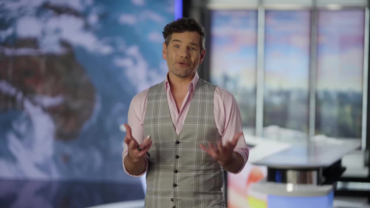 The man in the checkered vest gestures with his hands, speaking to the camera. Behind him, a blurred map of the world is visible, typical of ABC Australia news.
