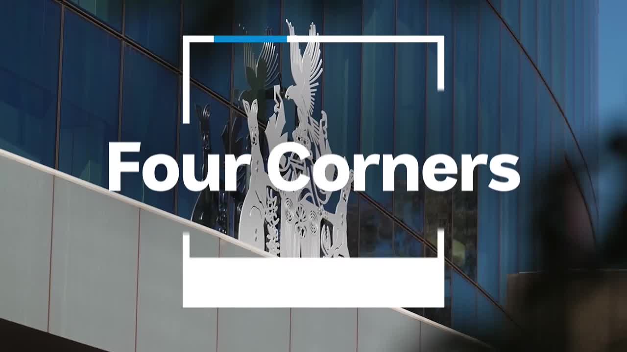 The words "Four Corners" are displayed in large white letters against a backdrop of a modern building. A metal sculpture of birds and figures stands out against the glass facade.
