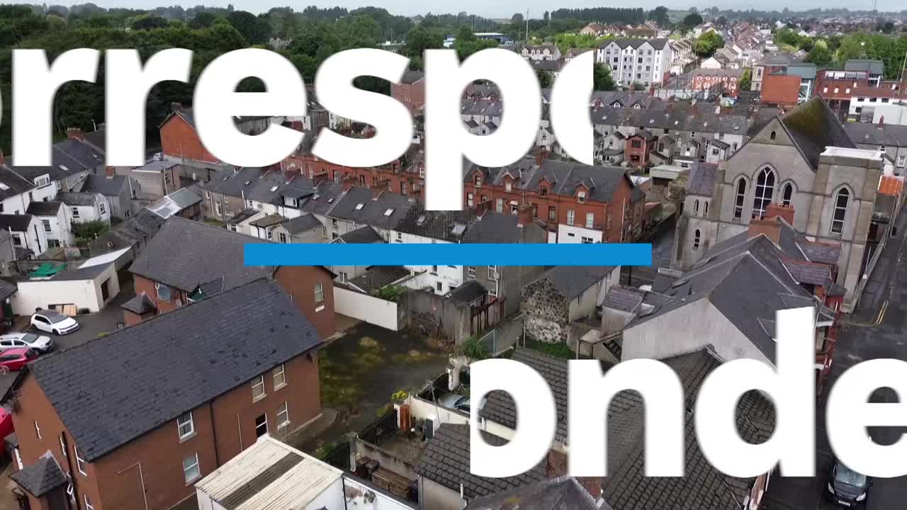 From this high angle, a townscape of rooftops and buildings stretches out under a cloudy sky, with a church spire standing tall. The ABC Australia news graphic partially obscures the view.
