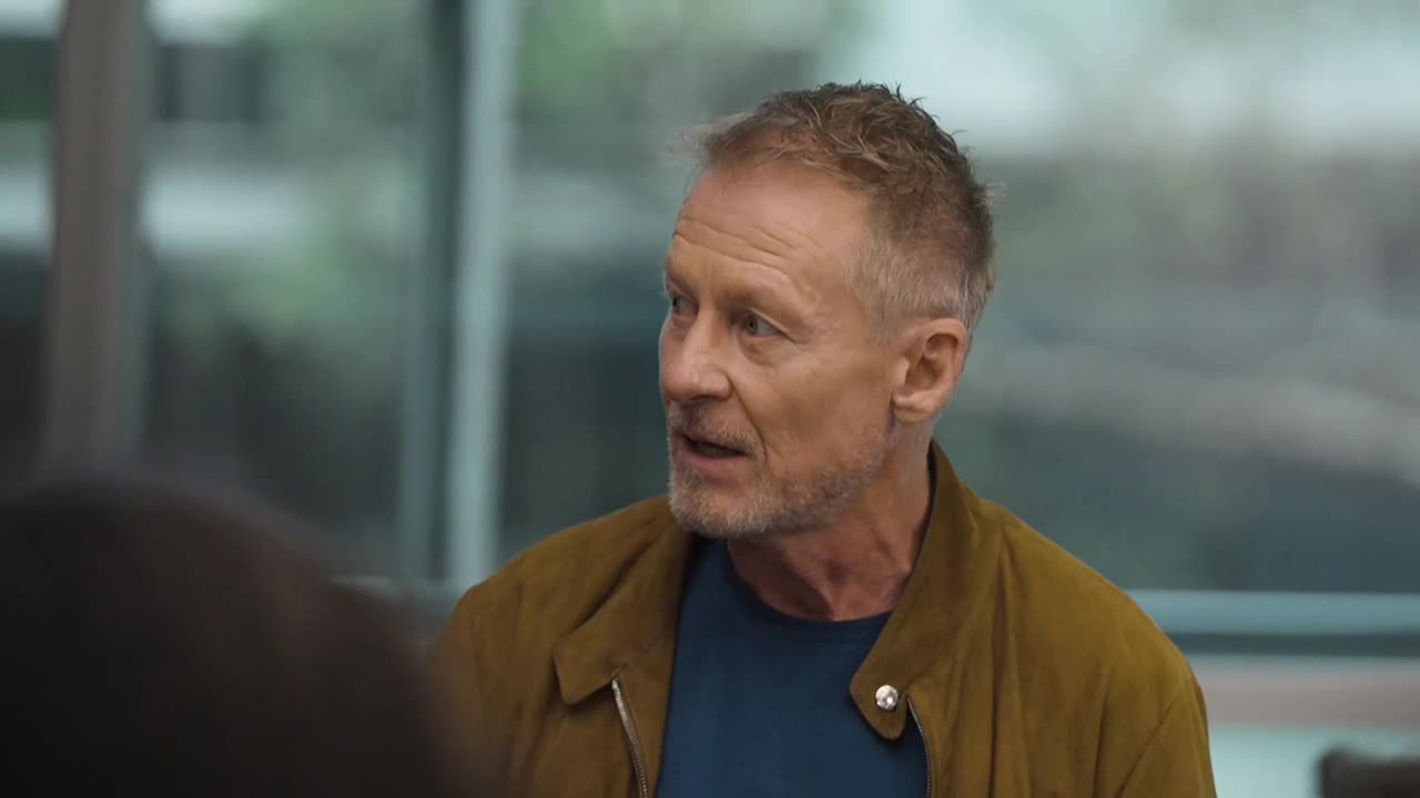 The man in the mustard-colored jacket is mid-sentence, his gaze fixed on someone out of frame. He's in a well-lit room, likely an interview setting for ABC Australia.
