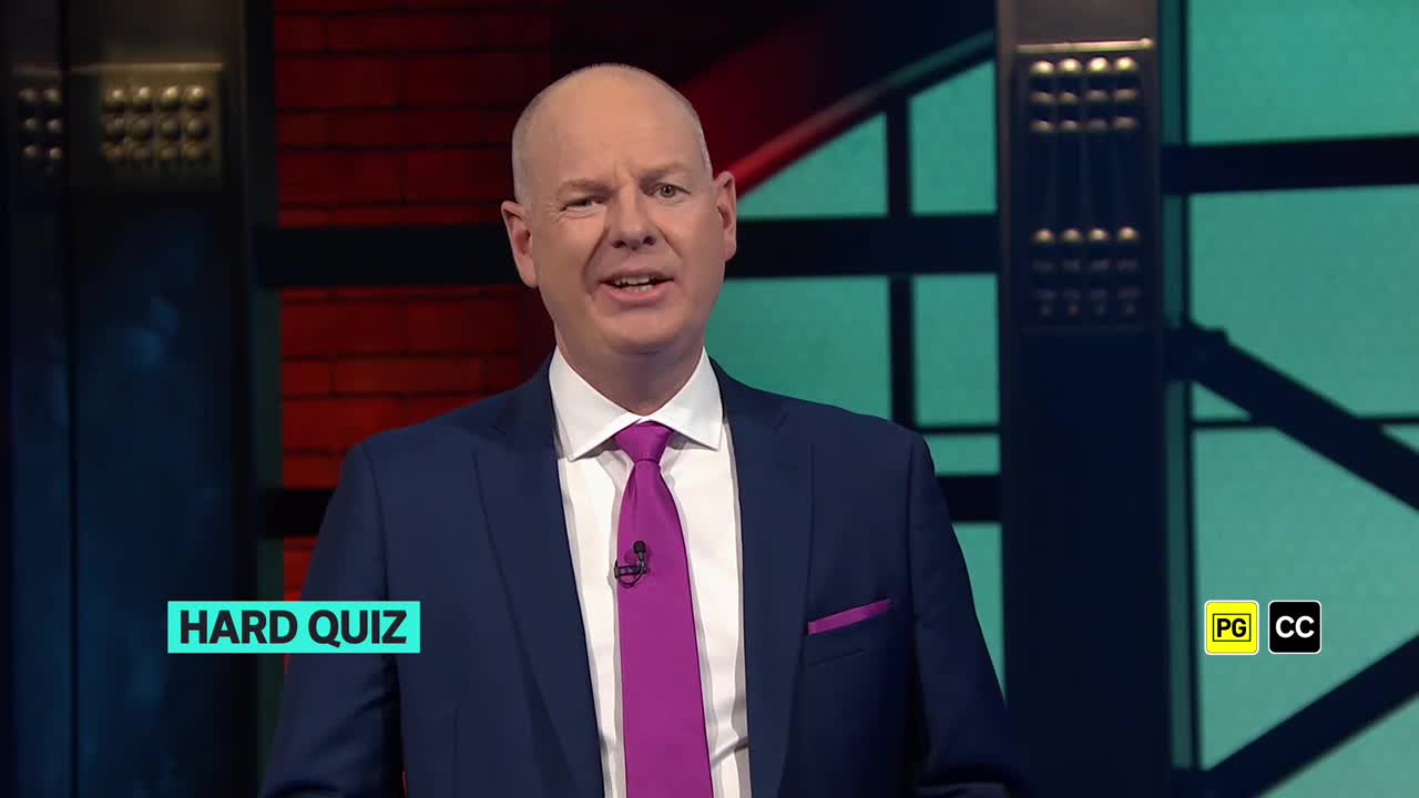The host, dressed in a navy suit and a bright purple tie, is speaking. A "Hard Quiz" title card is visible in the bottom left corner.
