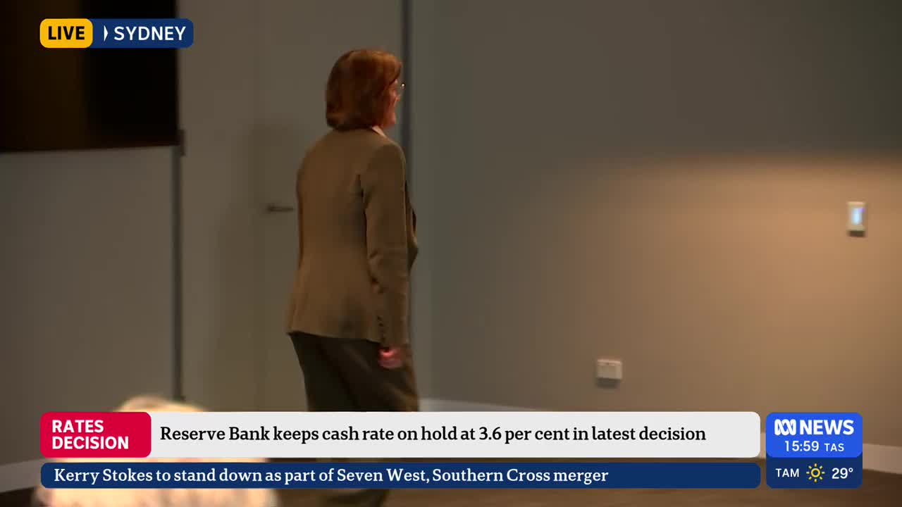 A woman in a brown blazer walks into the shot, her back to the camera. The ABC News banner at the bottom of the screen reports on the Reserve Bank's decision.
