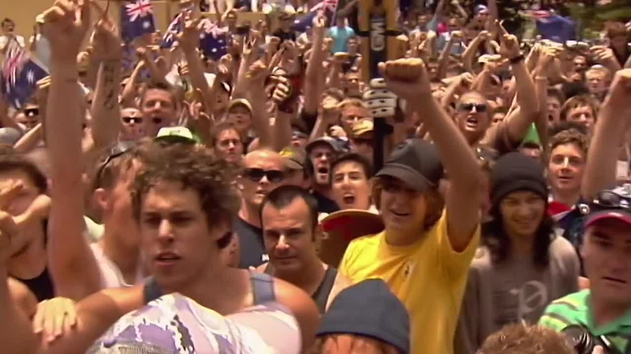 The crowd is packed tight, many with arms raised, fists clenched, and Australian flags waving above the heads. Faces are lit up with excitement, and the energy is palpable.
