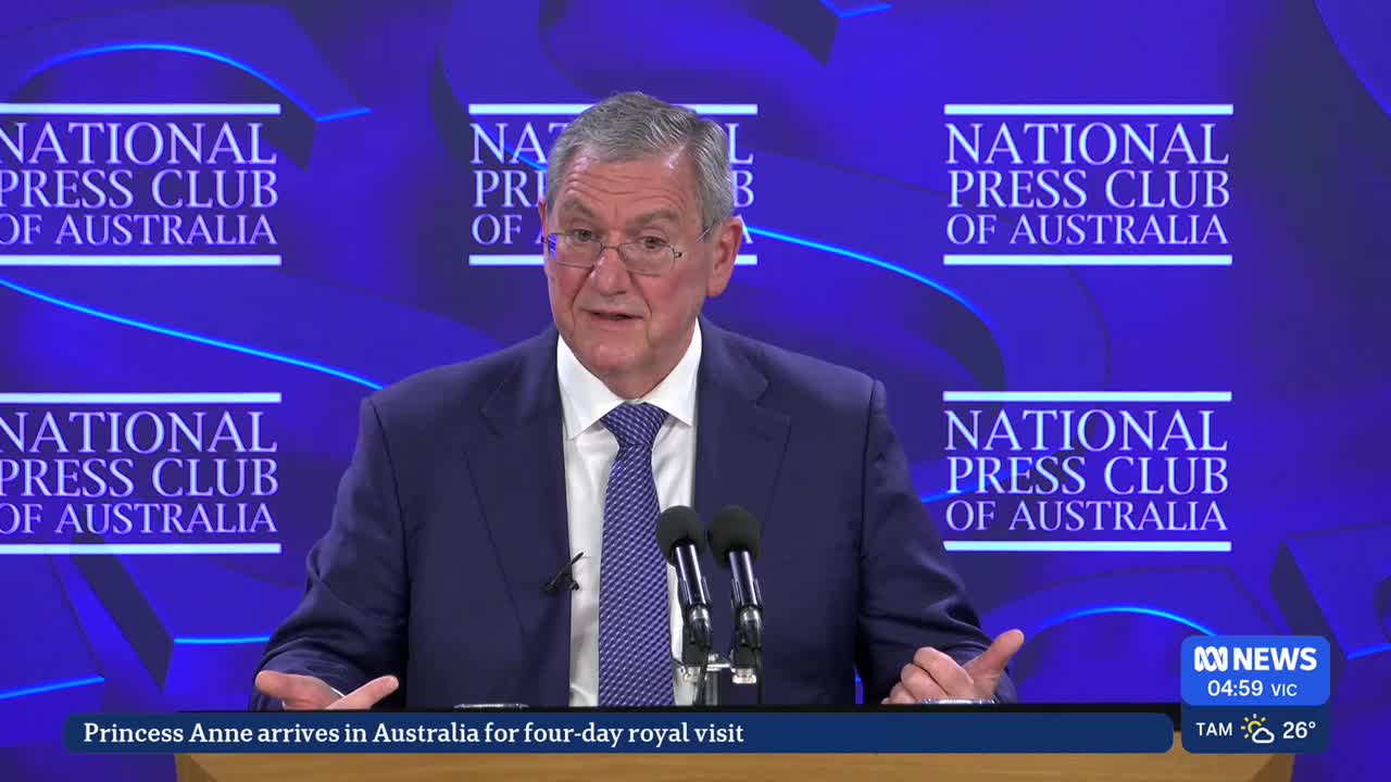 A man in a suit speaks into microphones at the National Press Club of Australia. ABC News is broadcasting the event, with a headline about Princess Anne's visit to Australia displayed at the bottom.
